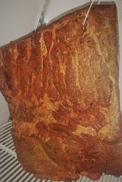 A large slab of seasoned meat roasting on a vertical spit, showcasing a crispy and golden-brown exterior, with the difference being its flavor enhanced by cold smoking.