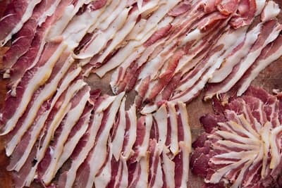 Sliced cured cold smoked bacon meats arranged neatly on a wooden surface.