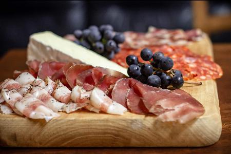 An appetizing charcuterie board featuring an assortment of cured meats, fresh grapes, and a wedge of brie cheese, elegantly displayed on a wooden serving platter.