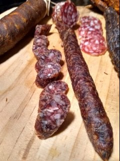 A selection of sliced cured sausages on a wooden board, showcasing the marbled texture of the meat inside.