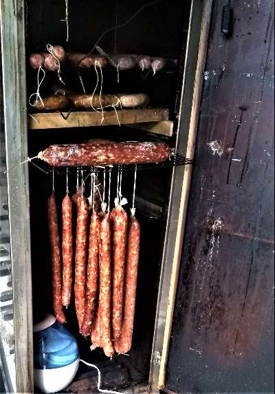 Homemade sausages hanging to cure inside a rustic wooden smoking cabinet.