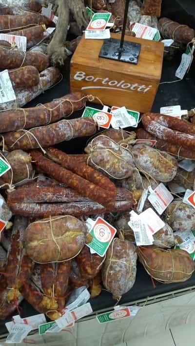 A selection of various cured meats, including cut salami, at a market, with a sign indicating the brand "Bertolotti.