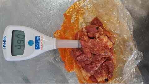 A digital thermometer displaying 69°f, inserted into a wrapped package of cured meats to check its temperature.