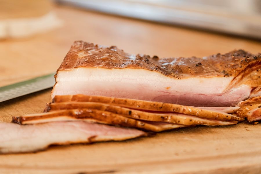 A close-up of perfectly sliced smoked bacon, revealing its moist and tender texture, ready to complement any hearty meal. Discover the art through our Cured Meat Courses online.