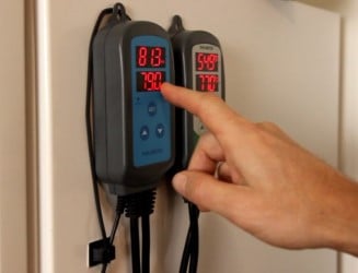A hand adjusting the INKBIRD ITC-308 temperature controller displaying detailed review readings.