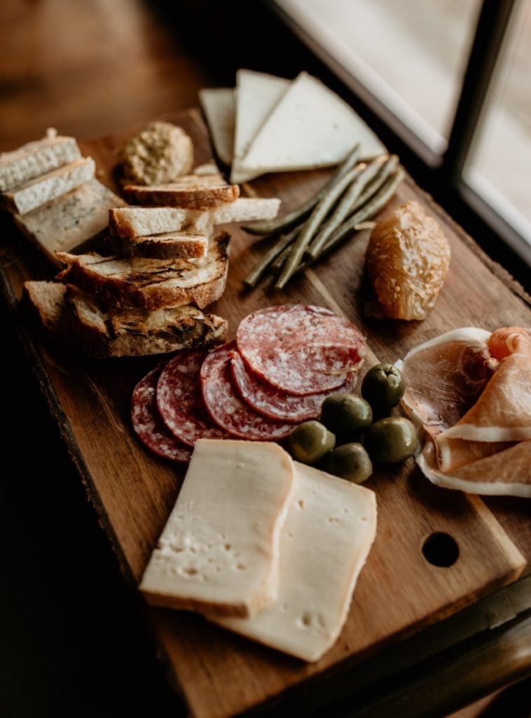 A rustic charcuterie board with an assortment of cheeses, cured meat, olives, bread, and green beans, ready for a delightful appetizer experience.