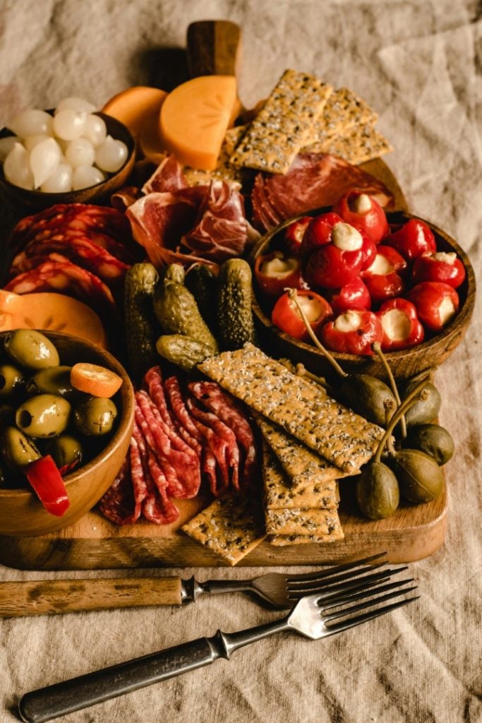 A rustic Charcuterie Board filled with an assortment of essentials like cured meat, cheeses, olives, pickles, and crackers, elegantly arranged for a delicious appetizer experience.