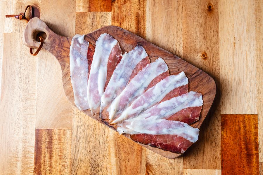 Thinly sliced cured meat served on a wooden cutting board.